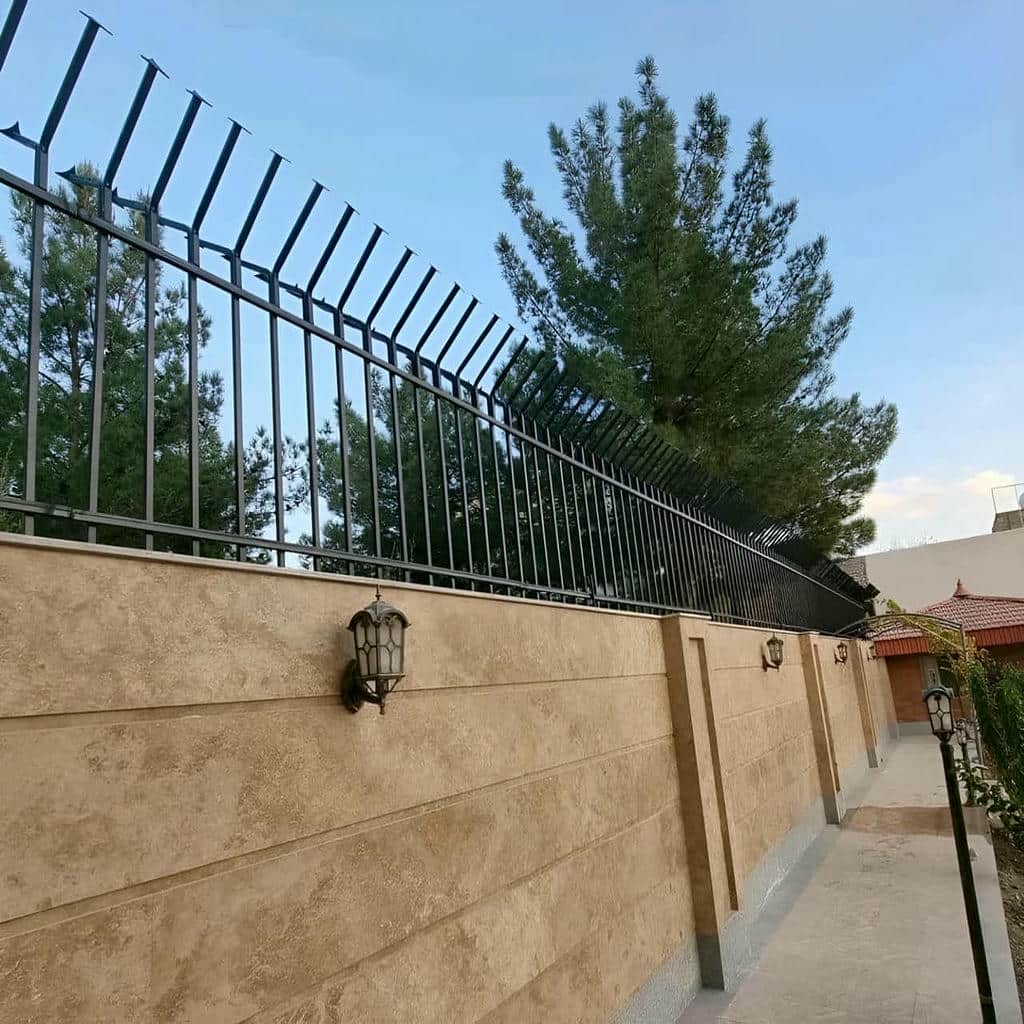 نرده سرنیزه ای خاکستری بر فراز دیوار آجری مجتمع